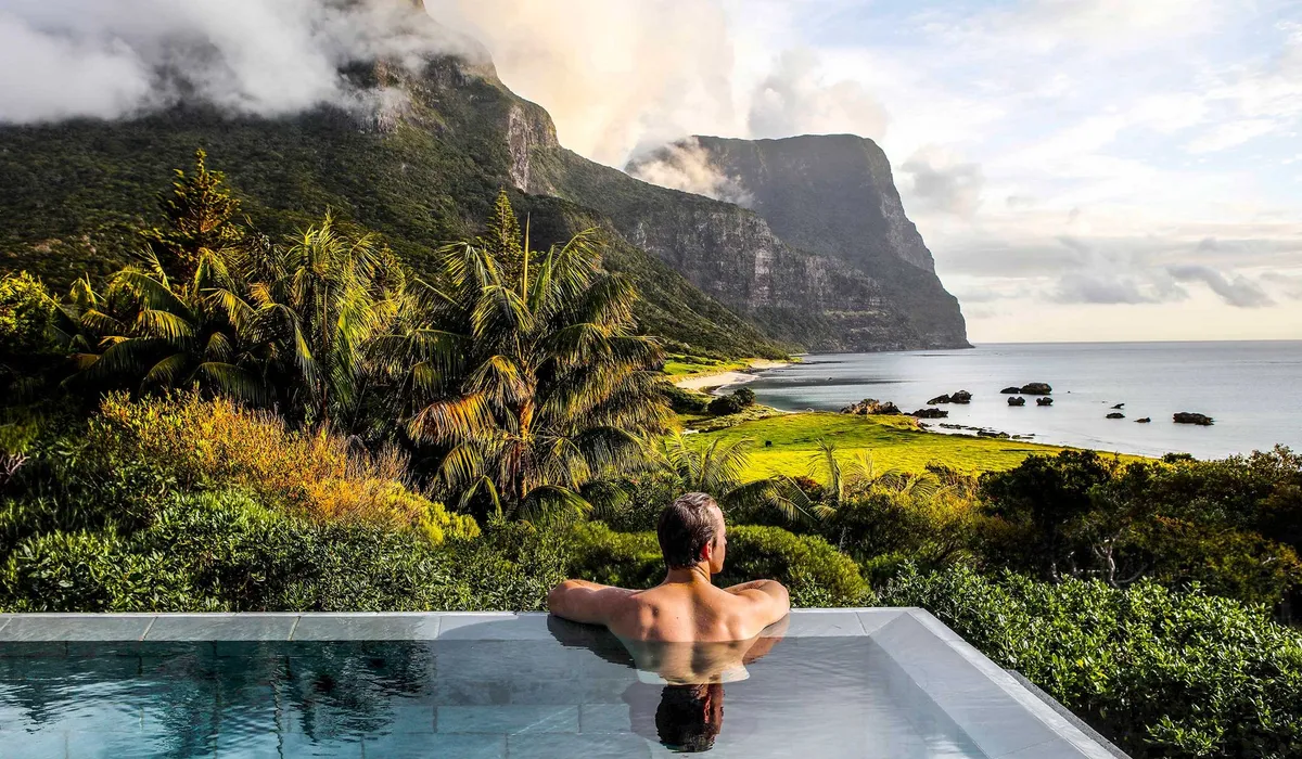 Capella Lodge: a guest in an infinity pool looking toward Mount Gower and Mount Lidgbird