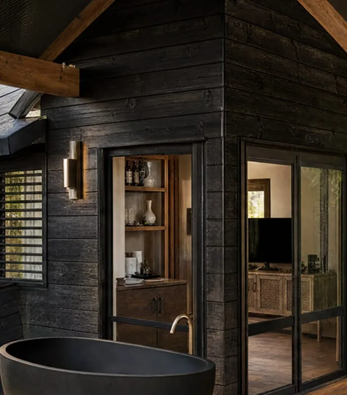 Artist's impression of a dark timber pavilion wall with a freestanding stone bath and glass doors into a living room
