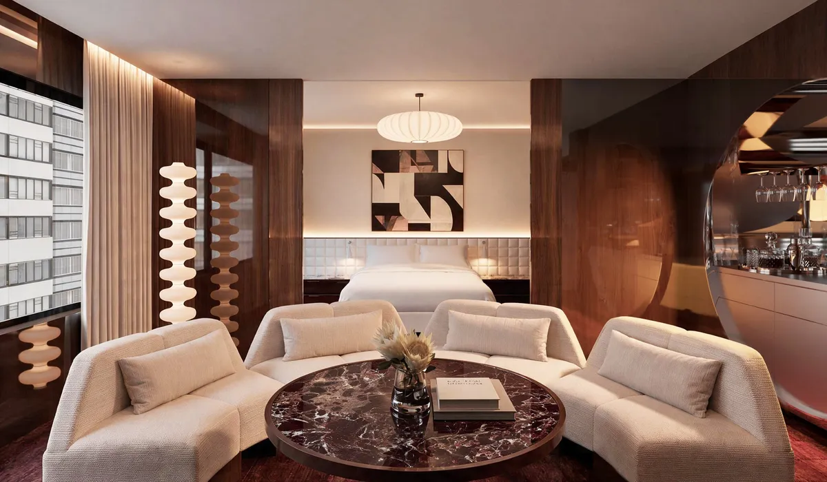 Render of a suite with a curved cream sofa around a burgundy marble table, and the bed behind
